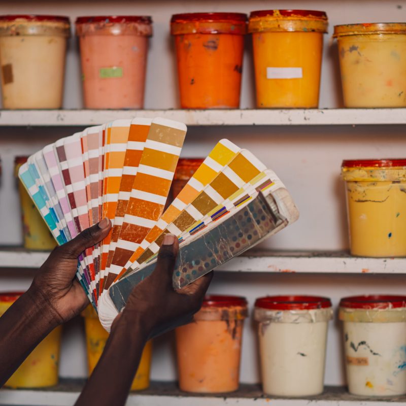 Close up of diverse graphic worker’s hands holding color swatch at factory Cropped picture of unrecognizable multicultural graphic worker's hands holding color swatch and choosing ink buckets from a shelf. Close up of diverse female graphic technology expert choosing colors.